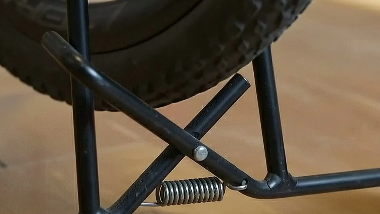 Close-up of the stand's sprung X-frame beneath a mounted wheel, showing the self-adjusting mechanism.