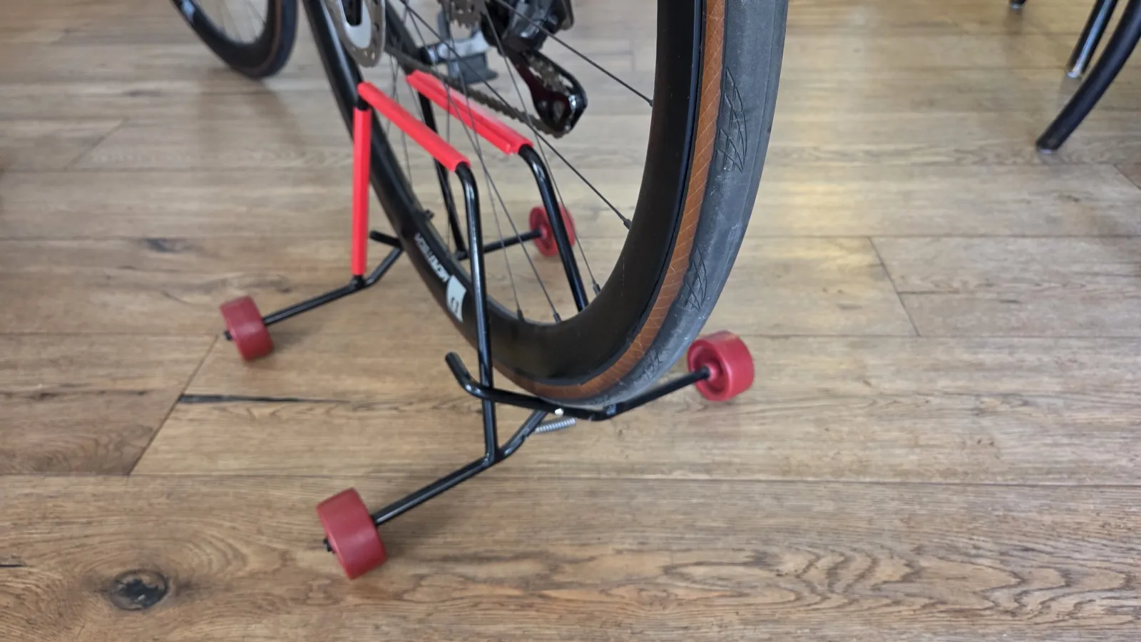 Road bike with tan-wall tyres upright in the Velaris stand on a timber floor.
